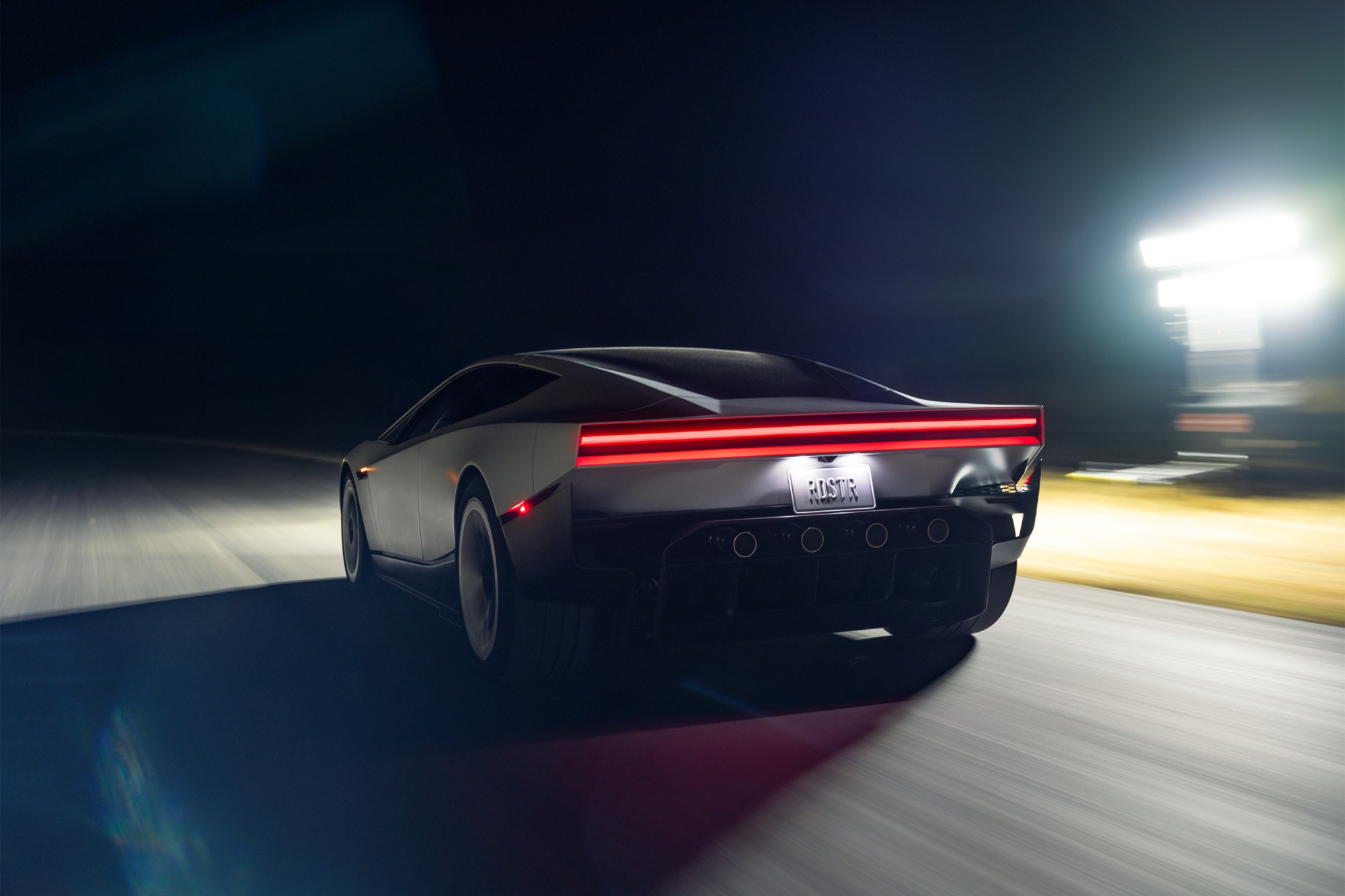 Rear view of the Roadster driving at night, its full-width red tail light glowing and the road blurred by speed